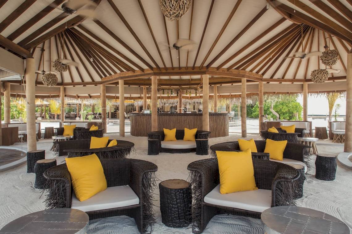 Loungebereich im Drift Thelu Veliga Retreat mit gelben Kissen und Korbstühlen.
