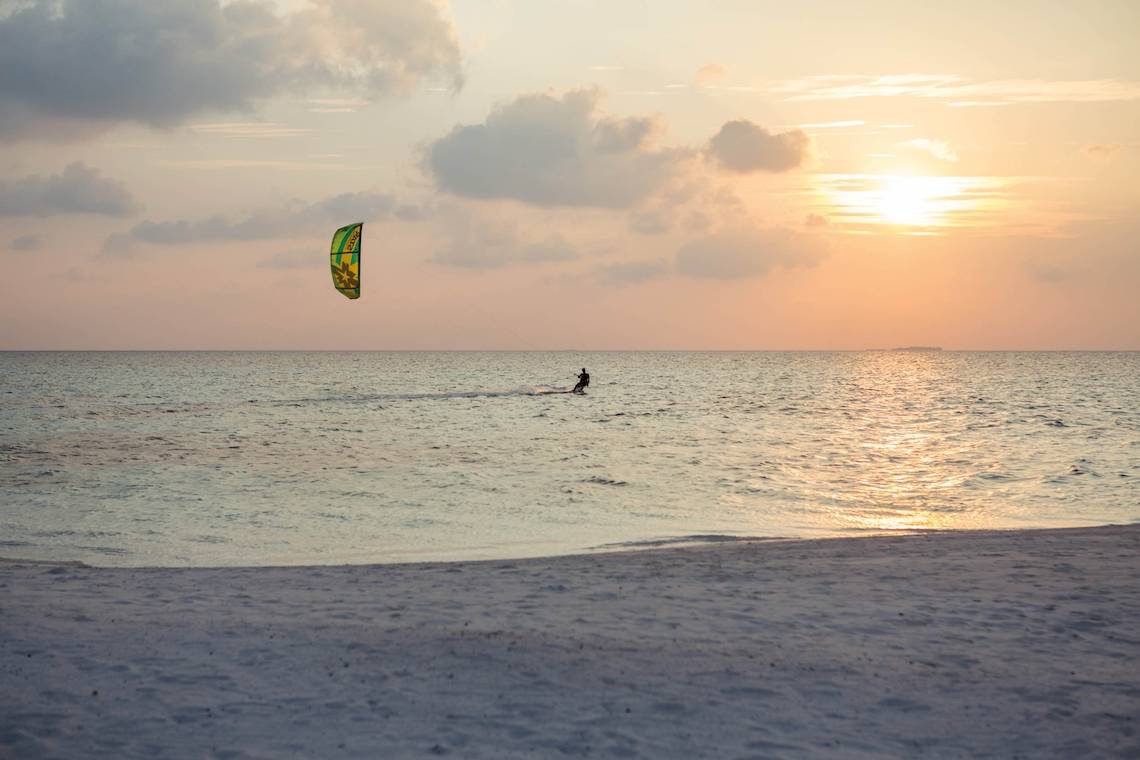 Sonnenuntergang am Strand mit einem Kitesurfer im Wasser.