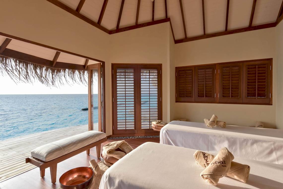 Massageraum im Drift Thelu Veliga Retreat mit Blick auf das Meer und zwei Massagetischen.