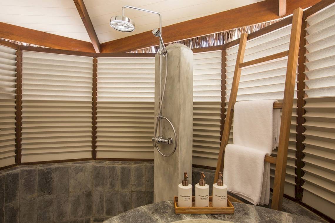 Ein Badezimmer mit einer Duschkabine und einem Holzständer mit Handtüchern im Drift Thelu Veliga Retreat.