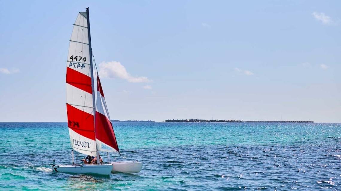Ein Segelboot mit rot-weißem Segel fährt im blauen Meer in der Nähe von Hurawalhi Island Resort.
