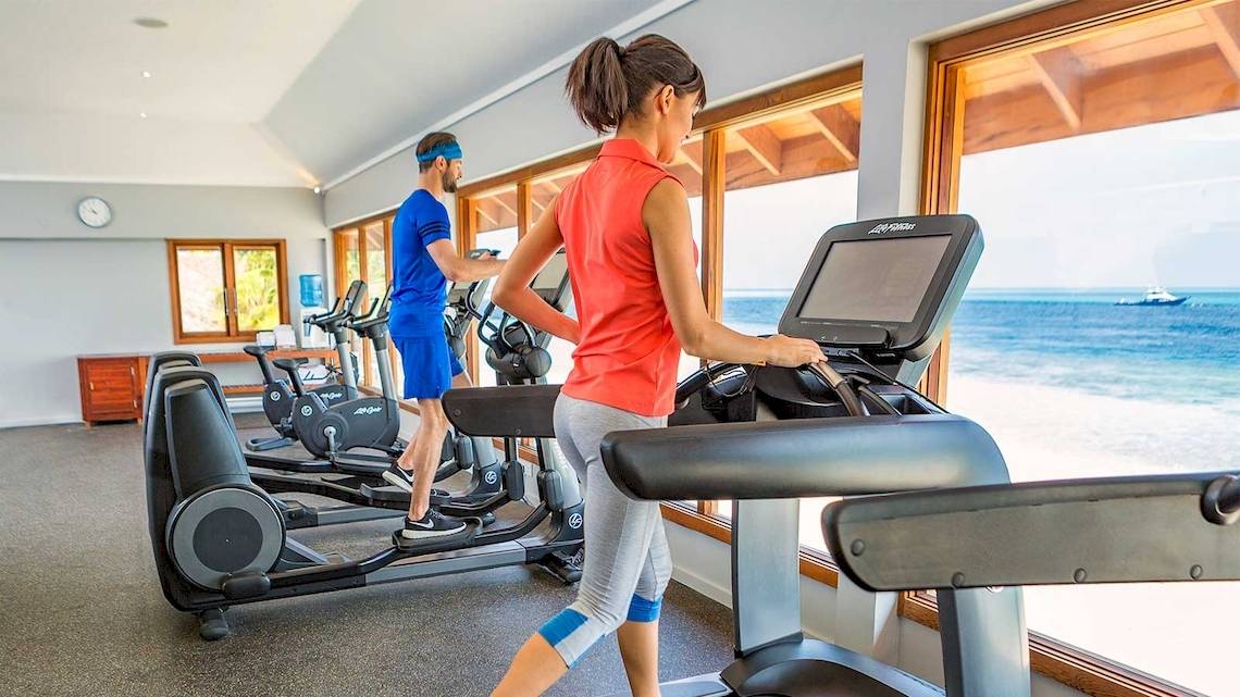 Fitnessstudio im Hurawalhi Island Resort mit zwei Personen auf Laufbändern und Blick auf das Meer.