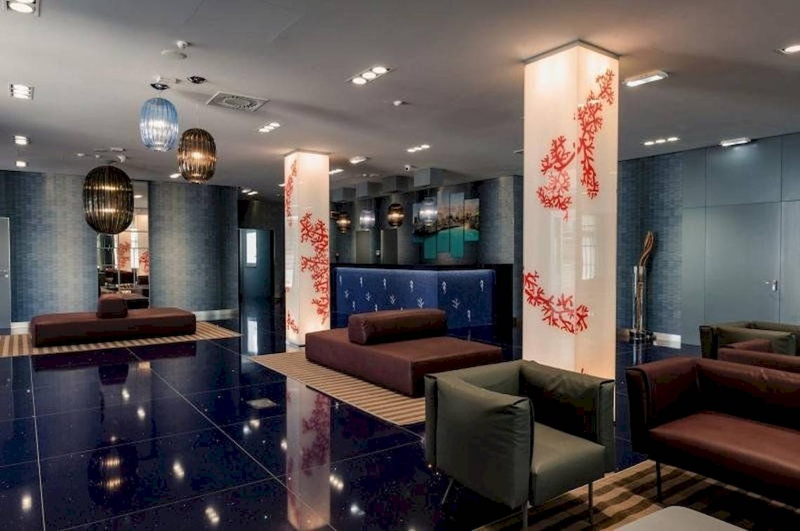 Lobby des Cala Ponte Hotels mit modernen Möbeln und blauen Wänden.
