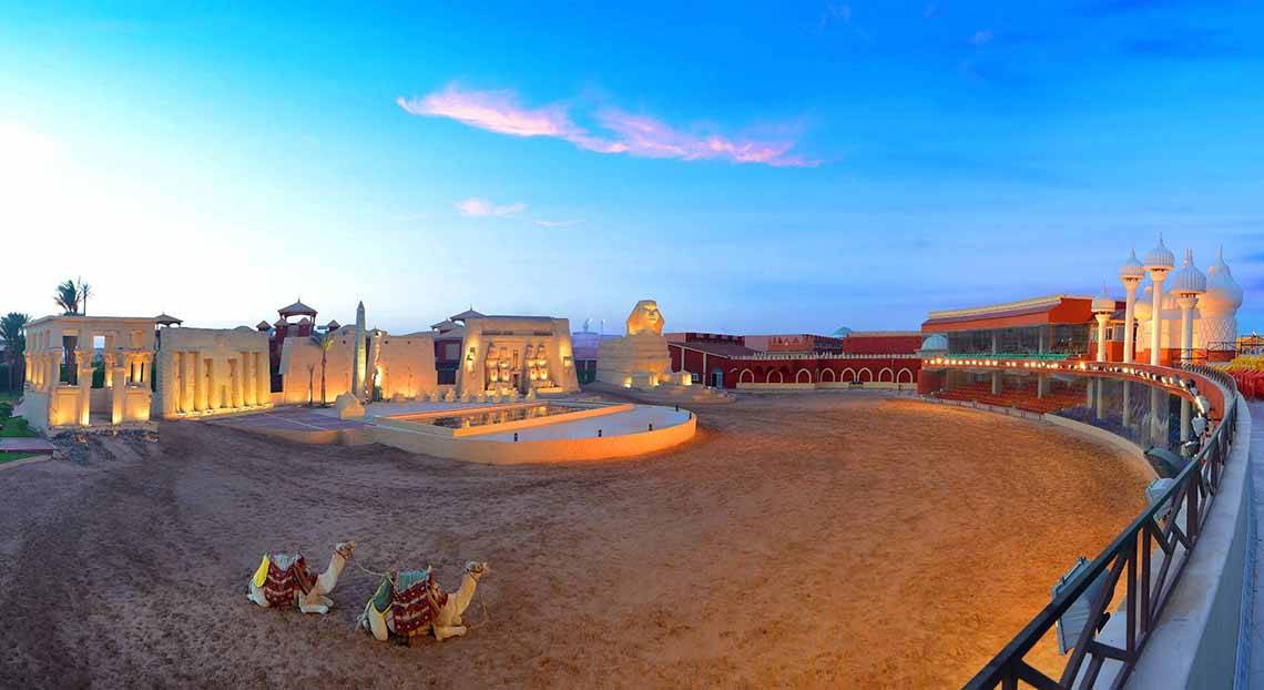 Außenansicht des Pickalbatros Alf Leila Wa Leila Resorts mit zwei Kamelen und einem Löwendenkmal bei Sonnenuntergang.