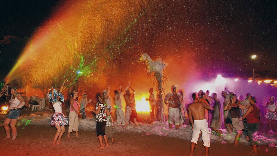 Gruppe von Menschen tanzt am Strand unter einem Feuerwerk und bunten Lichtern