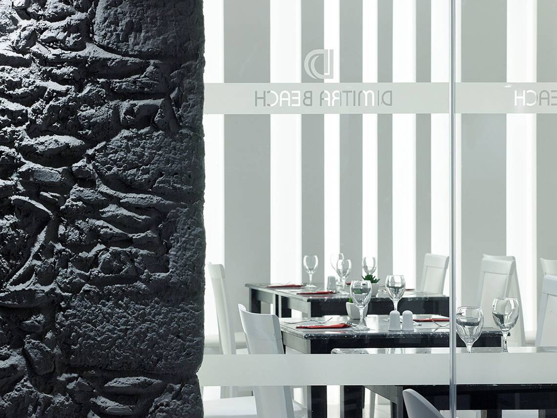 Innenansicht des Restaurants im Dimitra Beach Hotel & Suites mit schwarzen und weißen Tischplatten und weißen Stühlen.