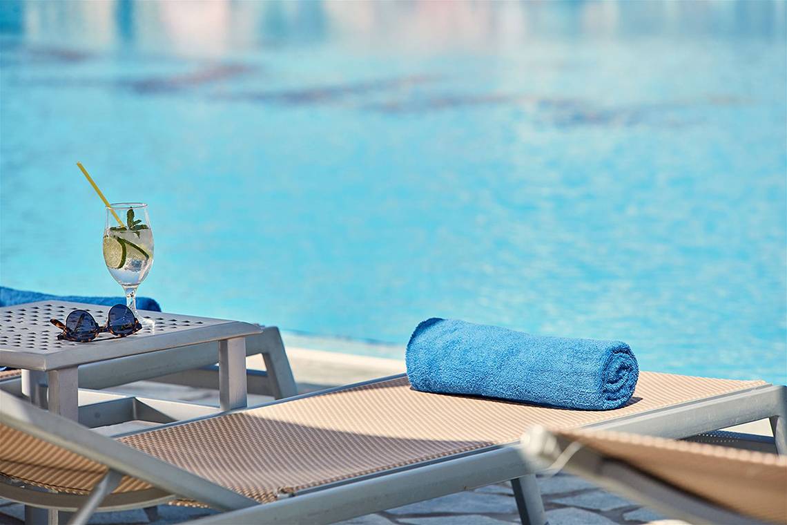 Ein Liegestuhlbereich am Pool mit einem Getränk und einem Handtuch.