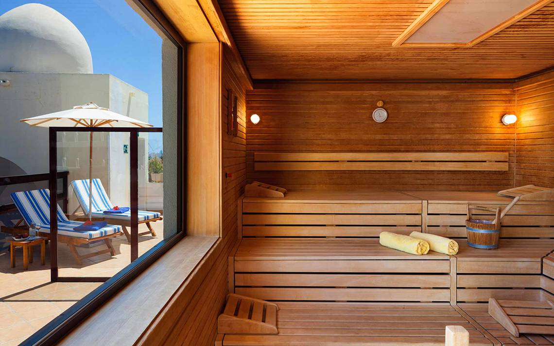 Innenansicht der Sauna im Seaside Sandy Beach Hotel mit Holzbänken, Fenster und Sonnenschirm.