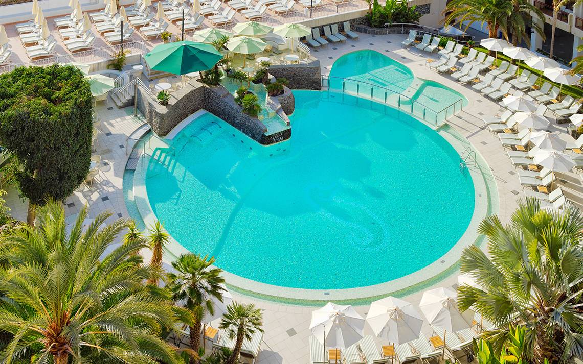 Luftaufnahme des Pools im Seaside Sandy Beach Hotel mit vielen Liegen und Sonnenschirmen.