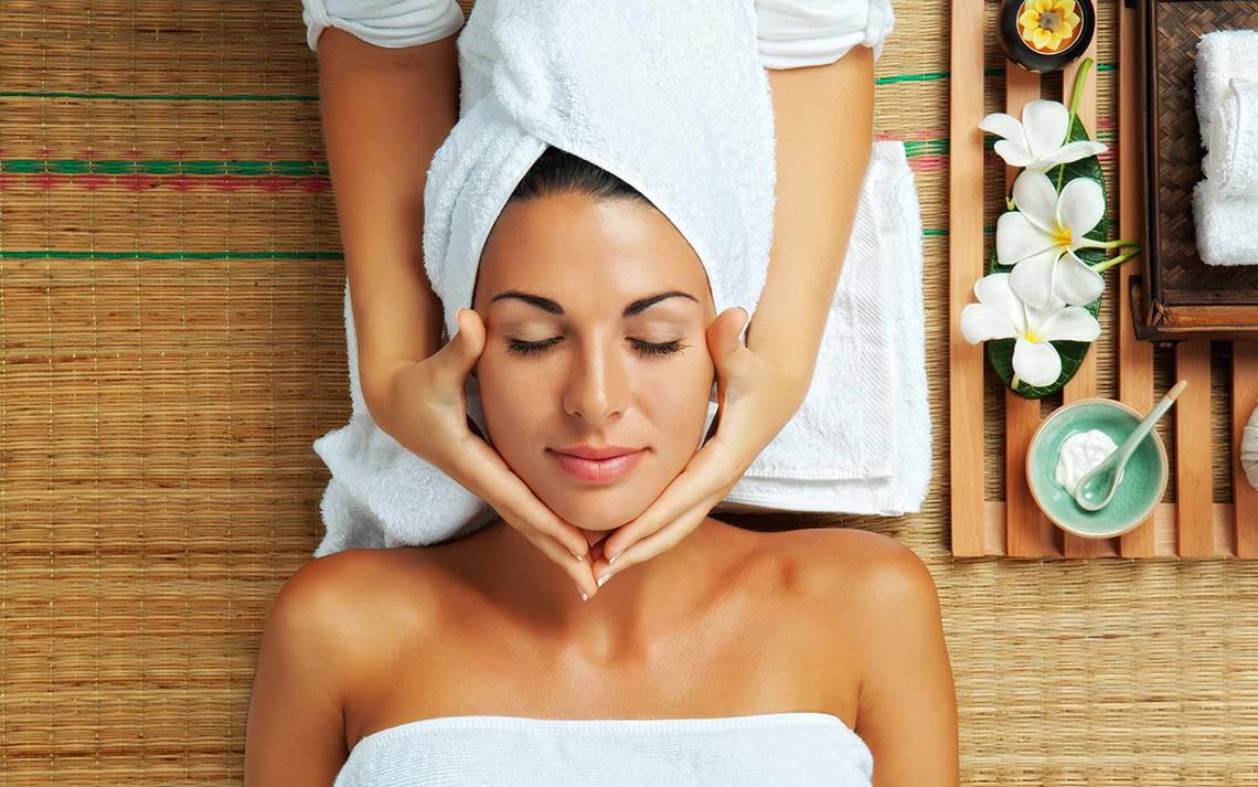 Frau im Spa-Salon mit einem Handtuch auf dem Kopf, die eine Gesichtsmassage genießt.