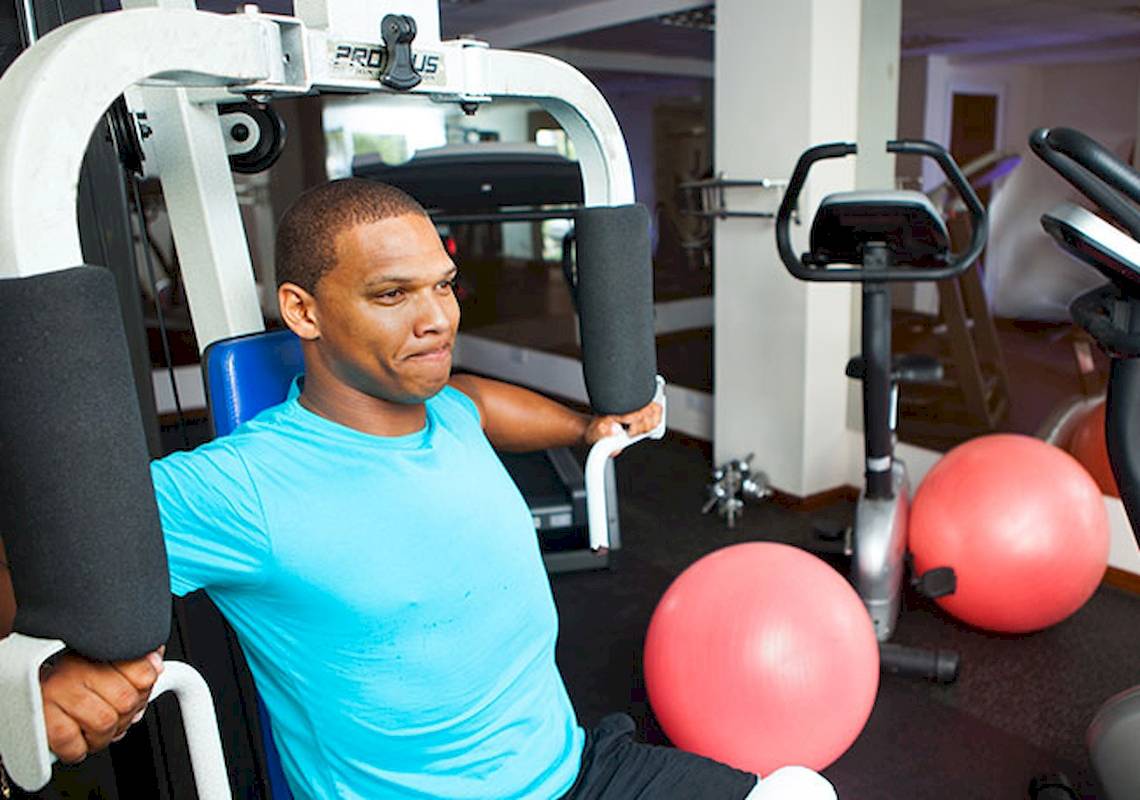 Mann im Fitnessstudio, der an einem Gerät arbeitet, umgeben von roten Gymnastikbällen.