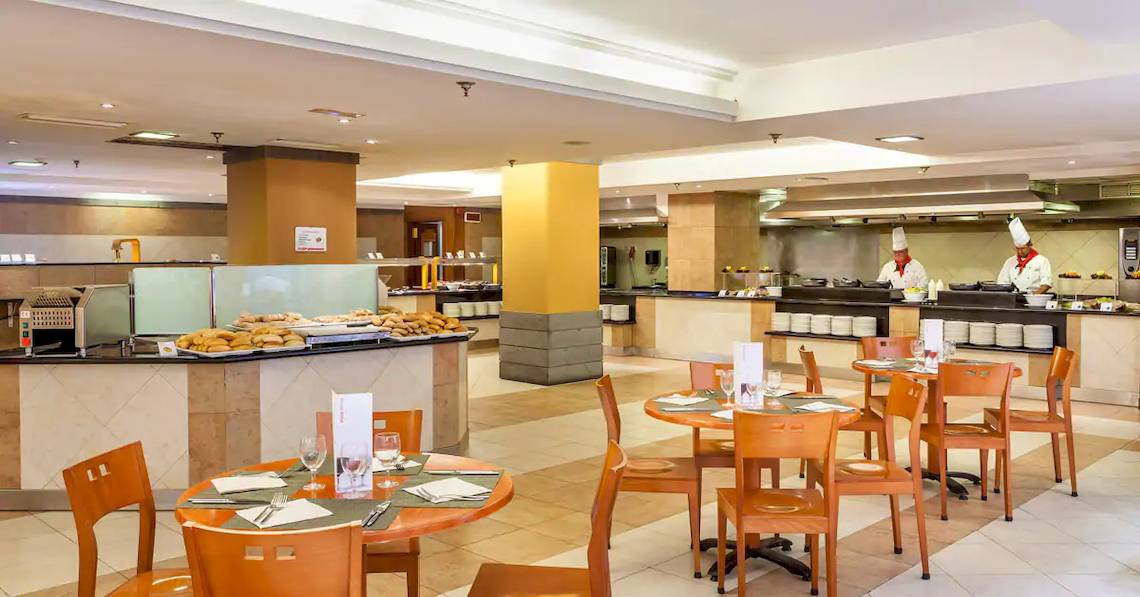 Innenansicht des Restaurants im Sol Tenerife Hotel mit gedeckten Tischen und Köchen hinter der Theke.