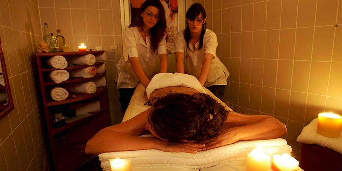 Eine Frau genießt eine Massage im Spa des Zora Hotels, während zwei Therapeutinnen sie betreuen.