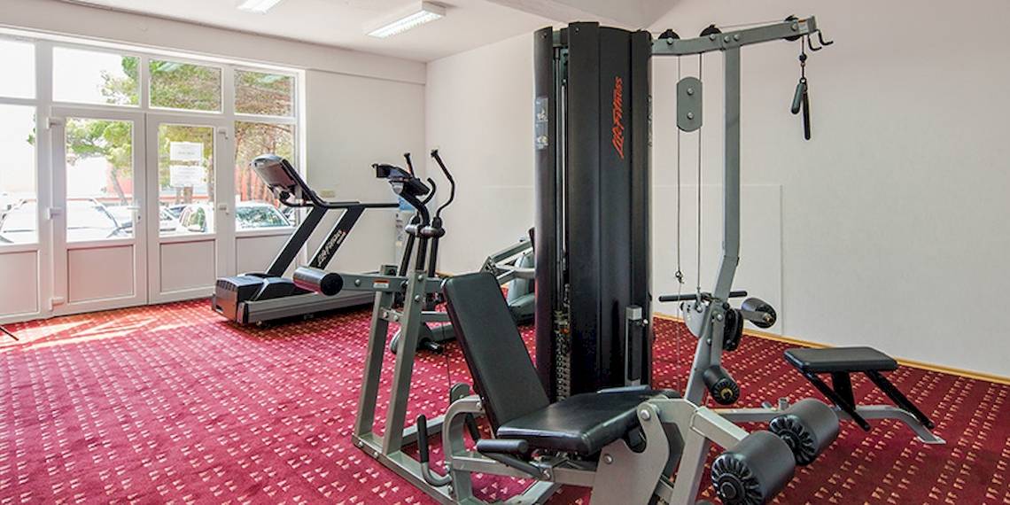 Fitnessraum im Zora Hotel mit Geräten und rotem Teppichboden.