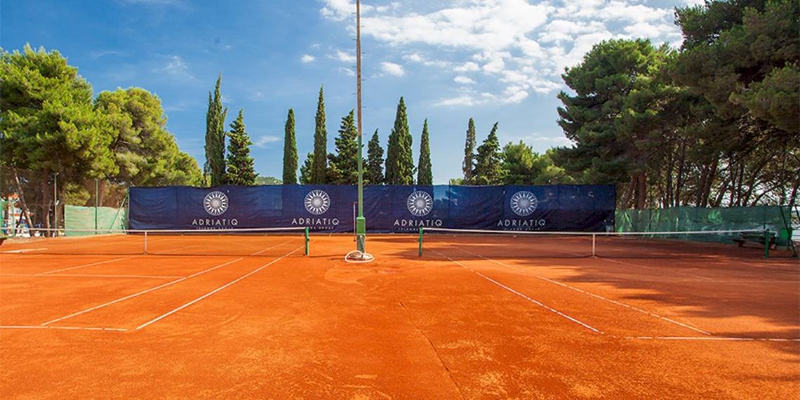 Tennisplatz im Zora Hotel mit blauen Bannern und Bäumen im Hintergrund.