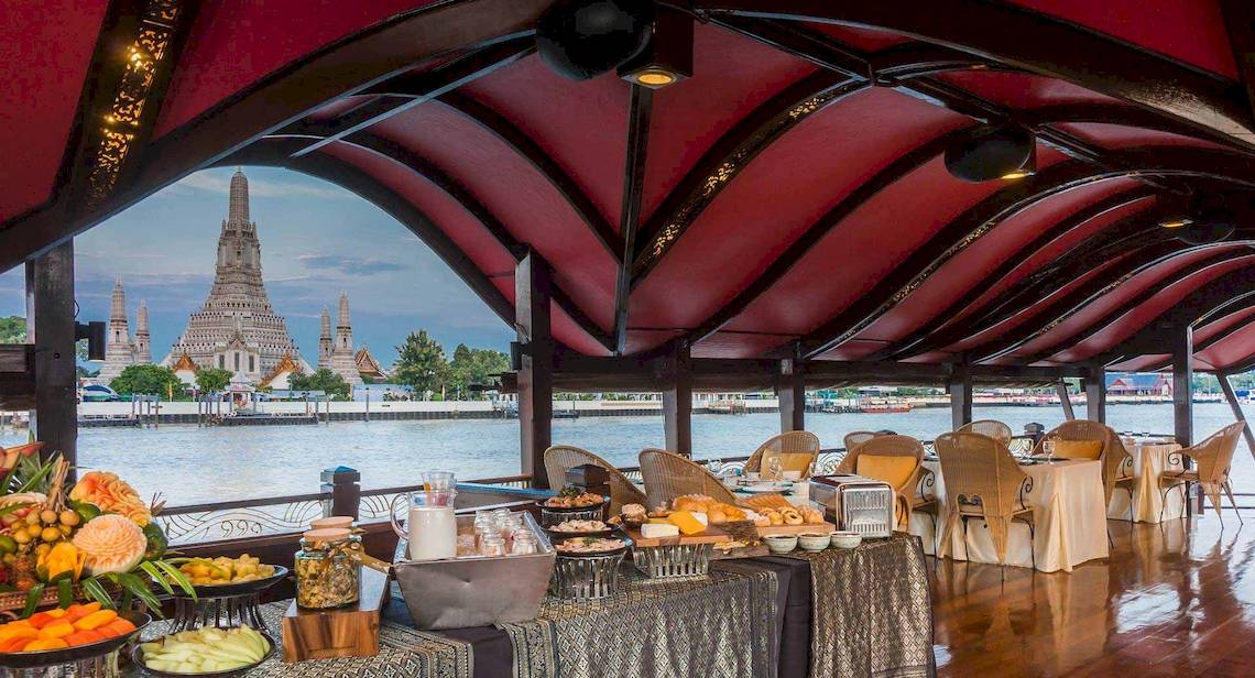 Innenbereich des Anantara Riverside Bangkok Resort mit einem Buffet und Aussicht auf den Fluss und den Tempel.