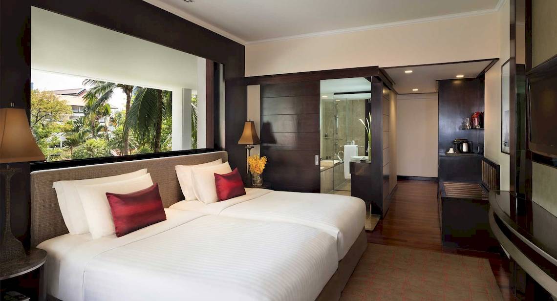 Doppelzimmer im Anantara Riverside Bangkok Resort mit zwei Betten, roten Kissen und einer Aussicht auf den Garten
