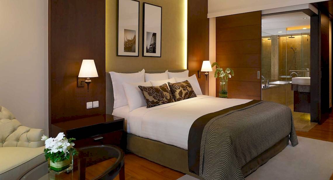 Schlafzimmer im Anantara Riverside Bangkok Resort mit Bett, Lampen und Möbeln.