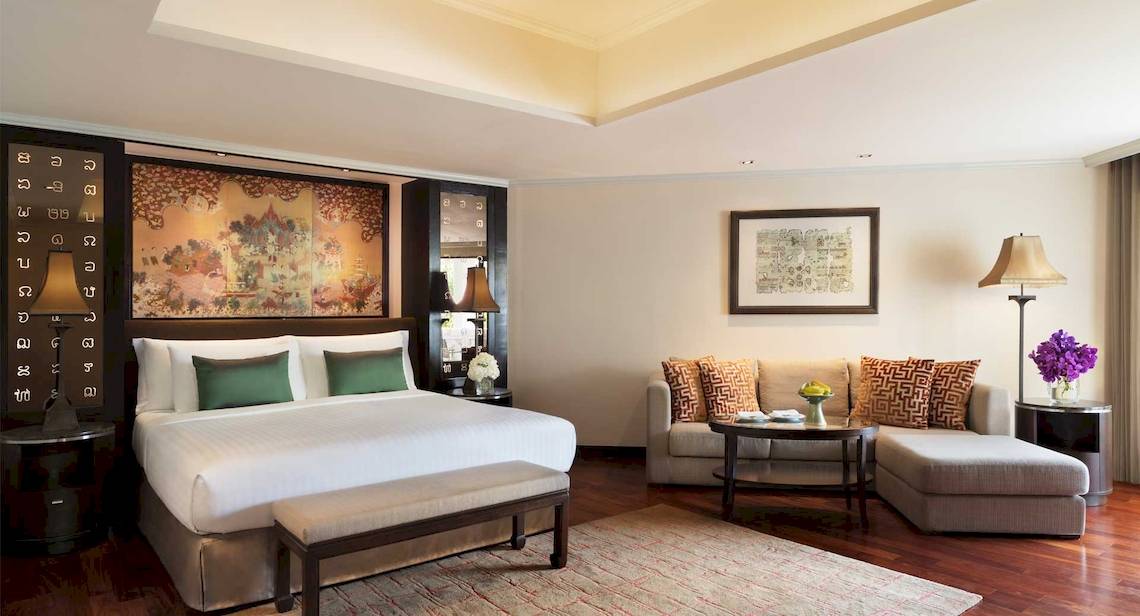 Ein elegantes Zimmer im Anantara Riverside Bangkok Resort mit einem großen Bett, einem Sofa und einer Tischlampe.