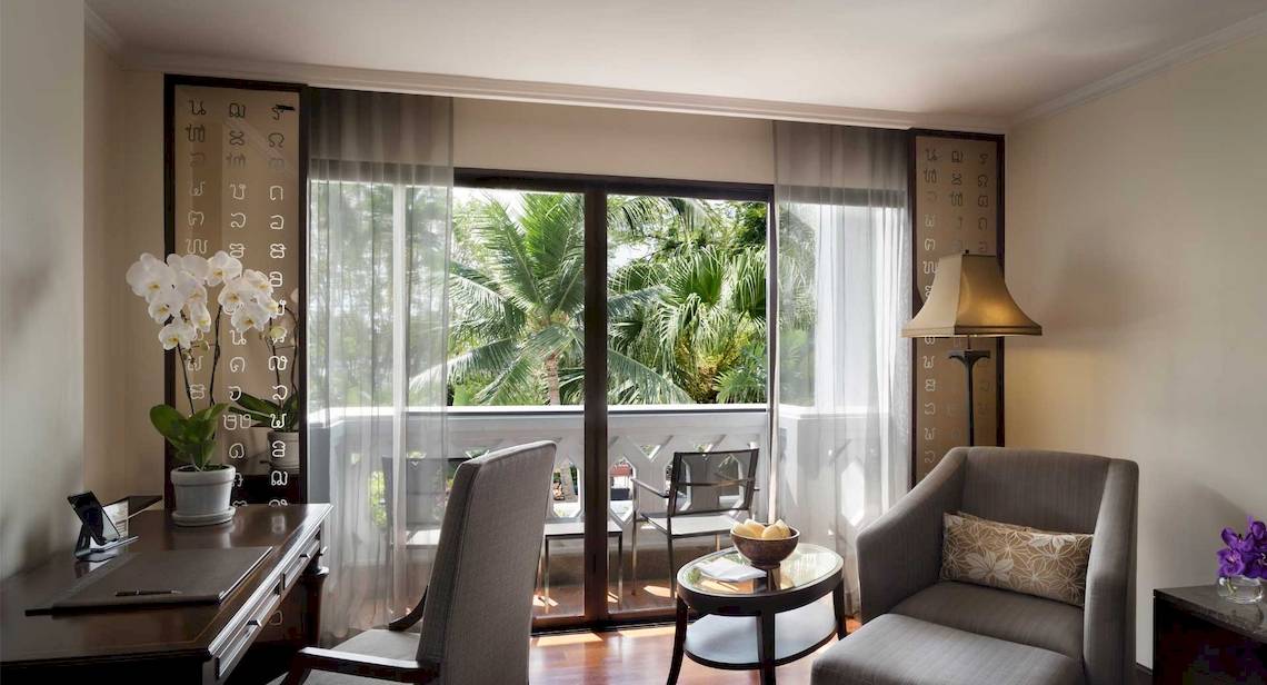 Innenansicht eines Zimmers im Anantara Riverside Bangkok Resort mit Schreibtisch, Stühlen und großem Fenster mit Balkon.