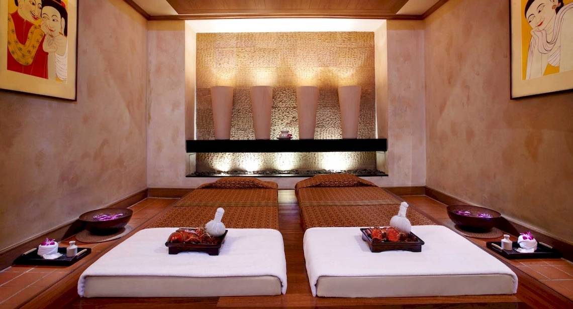 Behandlungsraum im Anantara Riverside Bangkok Resort mit zwei Massageliegen, gerahmten Bildern und Ambientbeleuchtung.