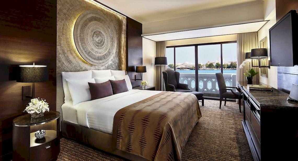 Innenansicht eines Zimmers im Anantara Riverside Bangkok Resort mit Bett, Möbeln und Blick auf den Fluss.