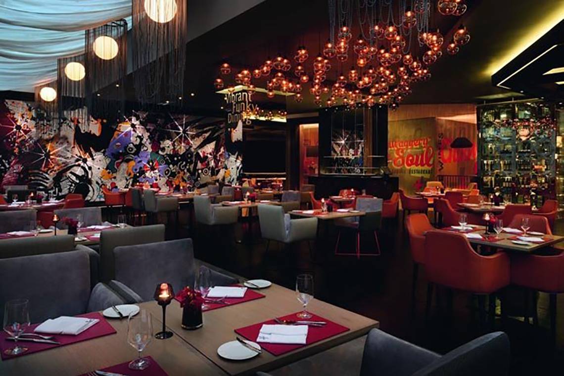 Innenansicht des Mövenpick Hotel Jumeirah Beach Restaurant mit bunten Wandgemälden und runden Tischen.