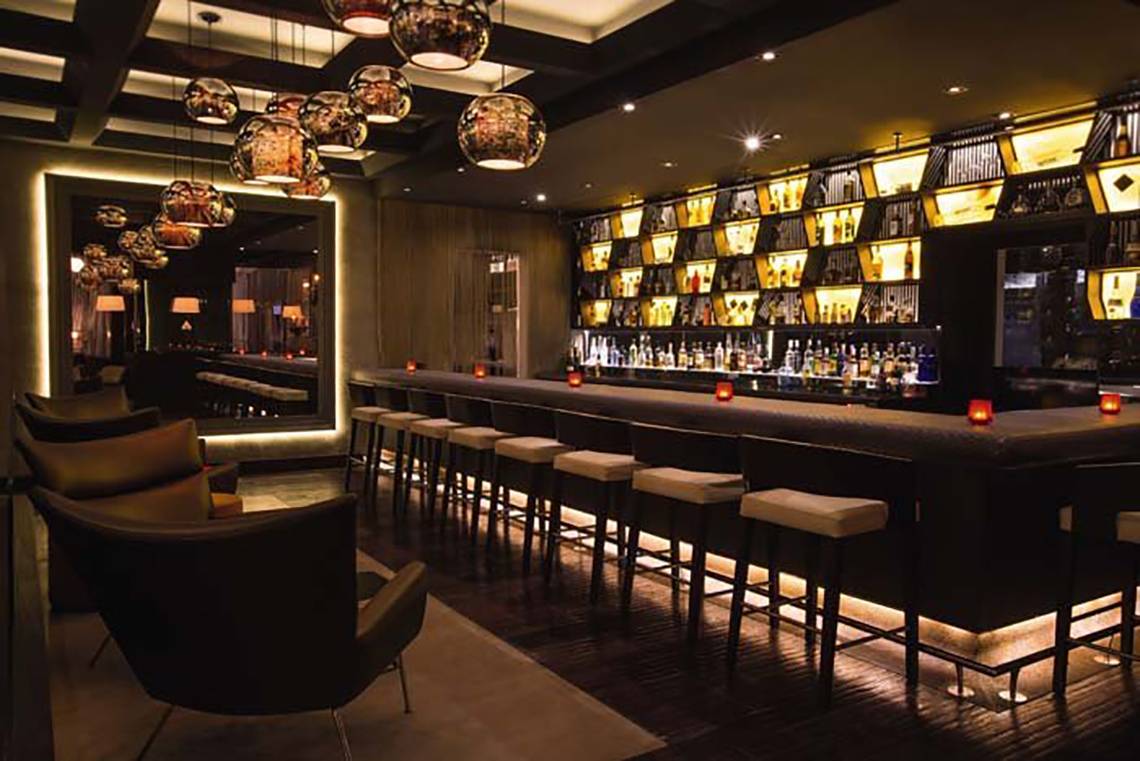 Barbereich im Mövenpick Hotel Jumeirah Beach mit gepolsterten Stühlen und beleuchteten Regalen.