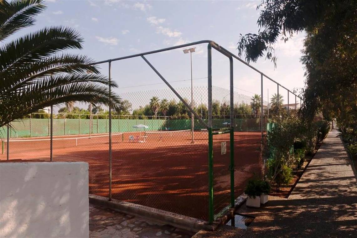 Tennisplatz im Atlantica Marmari Beach Hotel, umzäunt mit Pflanzen und Bäumen.