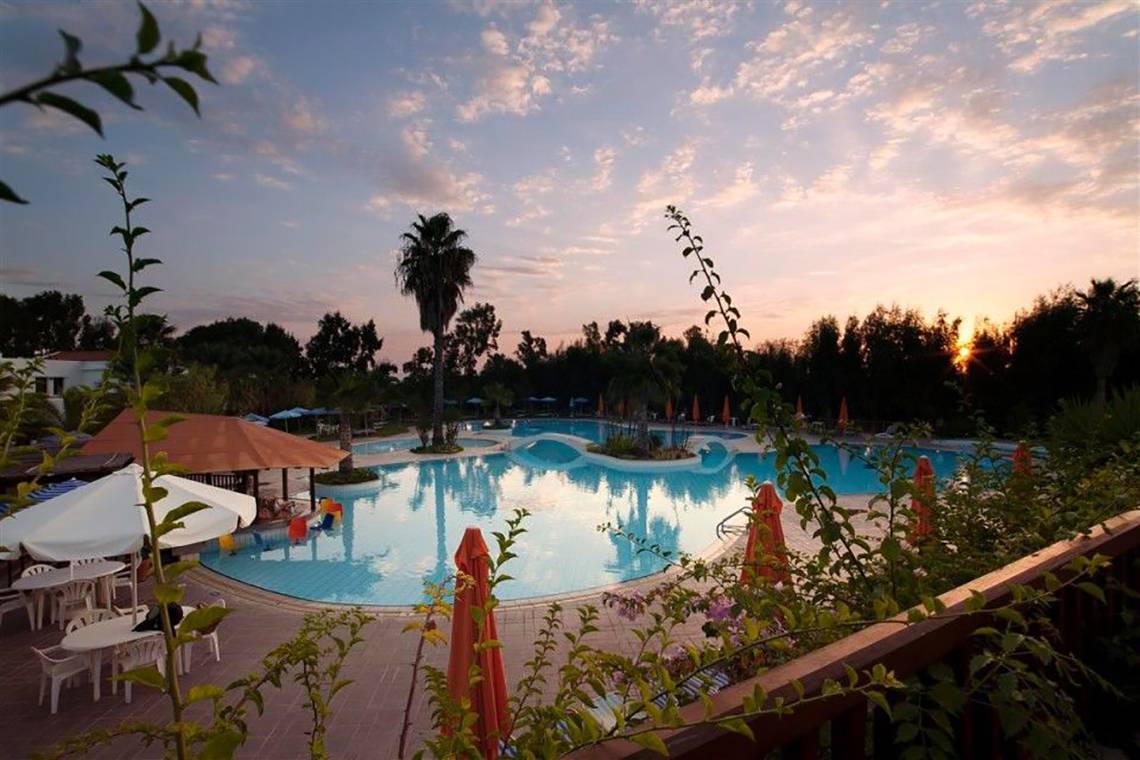Sonnenuntergang am Swimmingpool des Atlantica Marmari Beach Hotels mit blauem Wasser und weißen Sonnenschirmen.