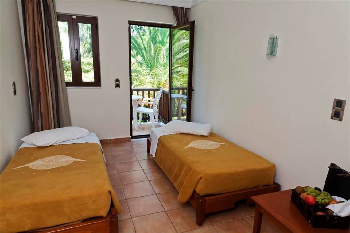 Zimmer mit zwei Betten und Balkon mit Blick auf den Garten im Atlantica Marmari Beach Hotel.