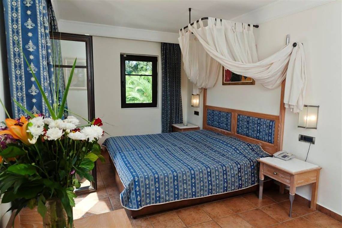 Schlafzimmer im Atlantica Marmari Beach Hotel mit blauen Vorhängen und Bettwäsche.
