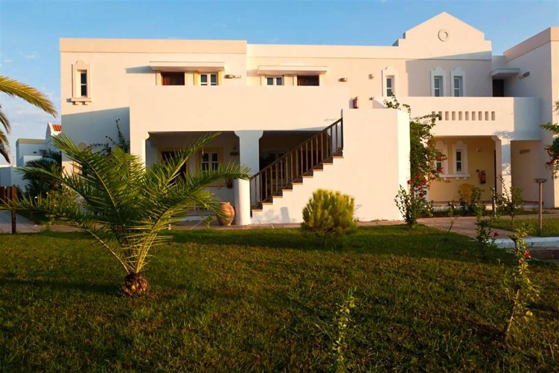 Außenansicht des Atlantica Marmari Beach Hotels mit grünem Rasen und Palme.