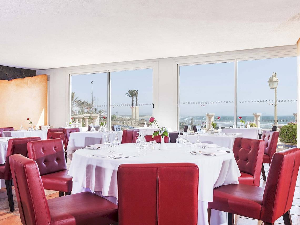 Innenansicht des Restaurants im Atlas Amadil Beach Hotel mit Blick auf das Meer und roten Stühlen.