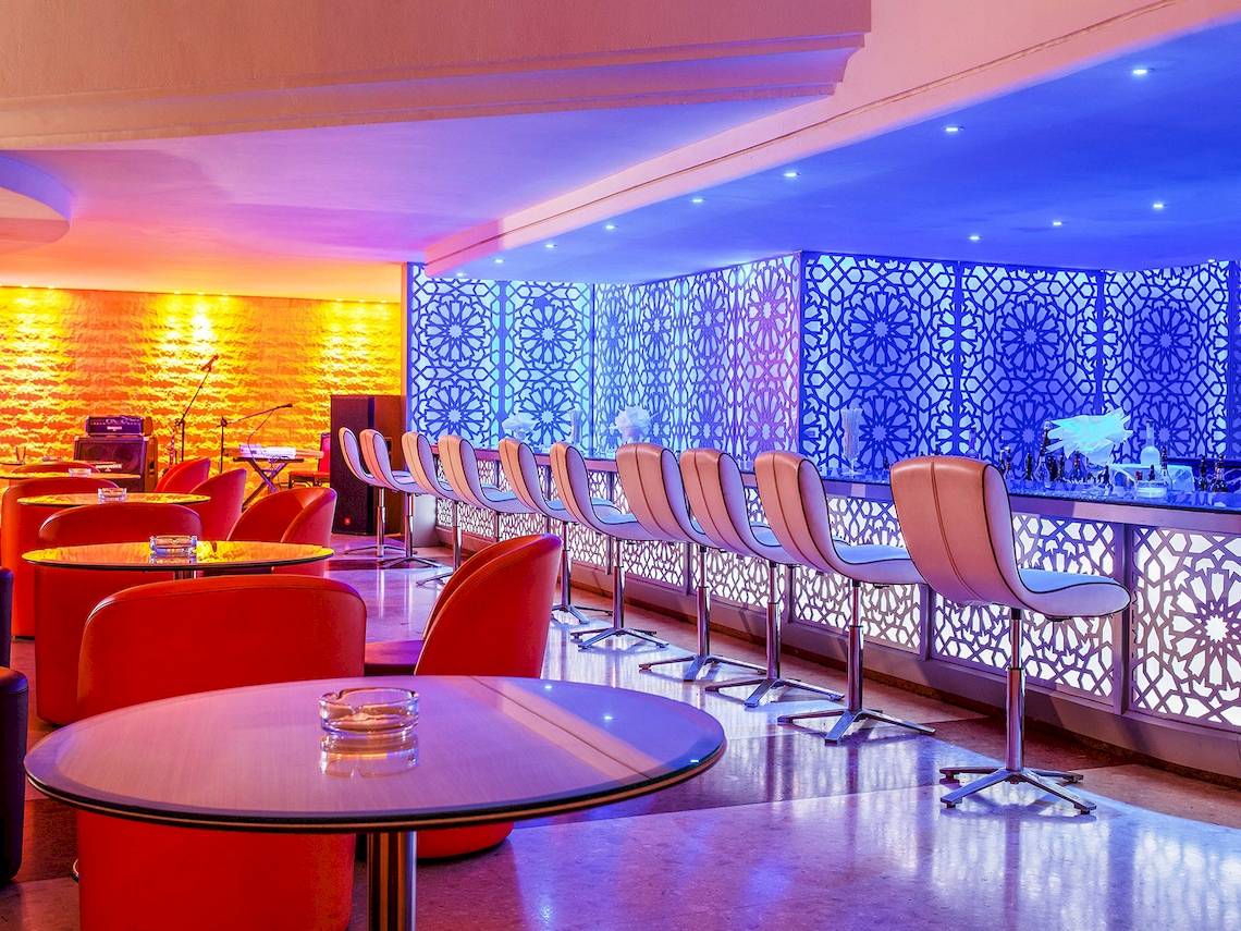 Barbereich des Atlas Amadil Beach Hotels mit roten Stühlen und blauer Beleuchtung.