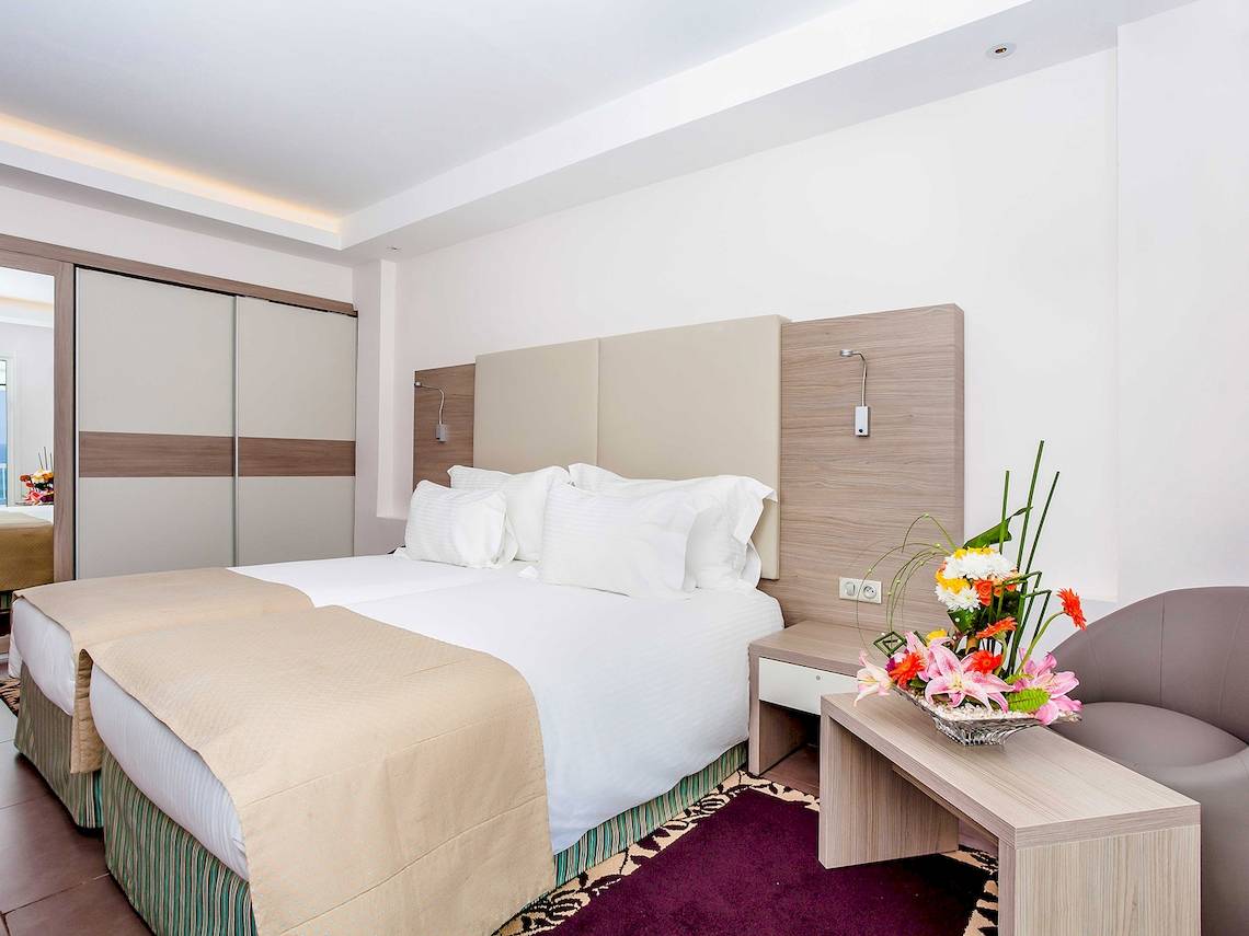 Schlafzimmer im Atlas Amadil Beach Hotel mit zwei Betten, weißen Kissen und einem Nachttisch mit Blumenvase.