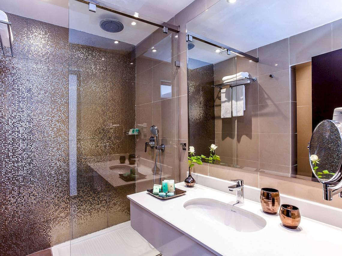 Badezimmer des Atlas Amadil Beach Hotels mit Glasdusche, Waschbecken und Spiegel.