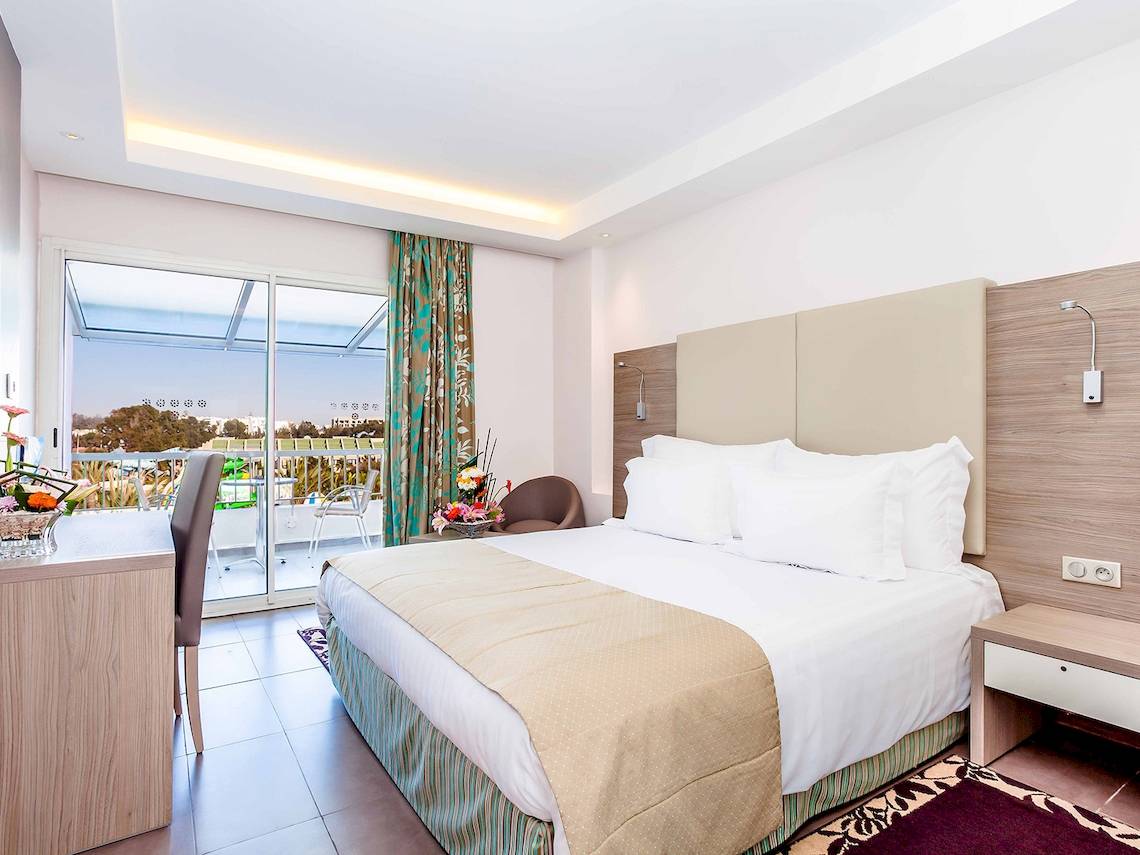 Innenansicht eines Hotelzimmers im Atlas Amadil Beach Hotel mit einem Bett, einem Schreibtisch und einem Balkon