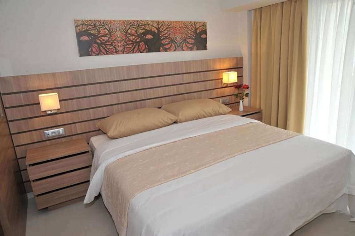 Ein Schlafzimmer im Atlantica Holiday Village Kos mit einem Doppelbett, zwei Nachttischen und Wandleuchten.