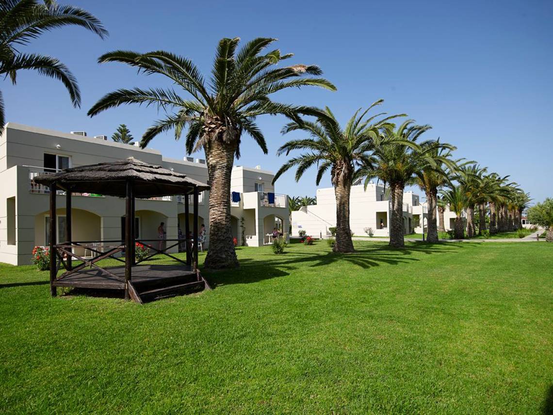 Außenbereich des Atlantica Holiday Village Kos mit Bungalows und Palmen.