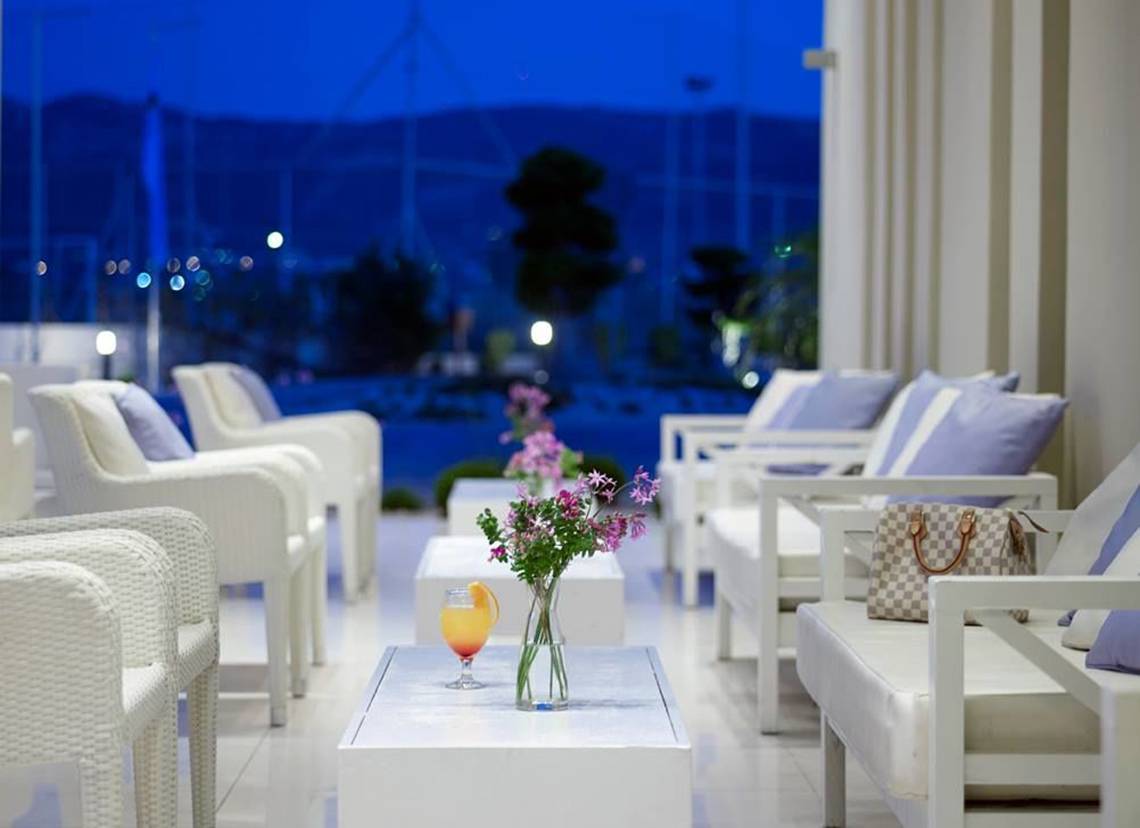 Loungebereich des Atlantica Holiday Village Kos mit weißen Möbeln und Blick auf einen Hafen.