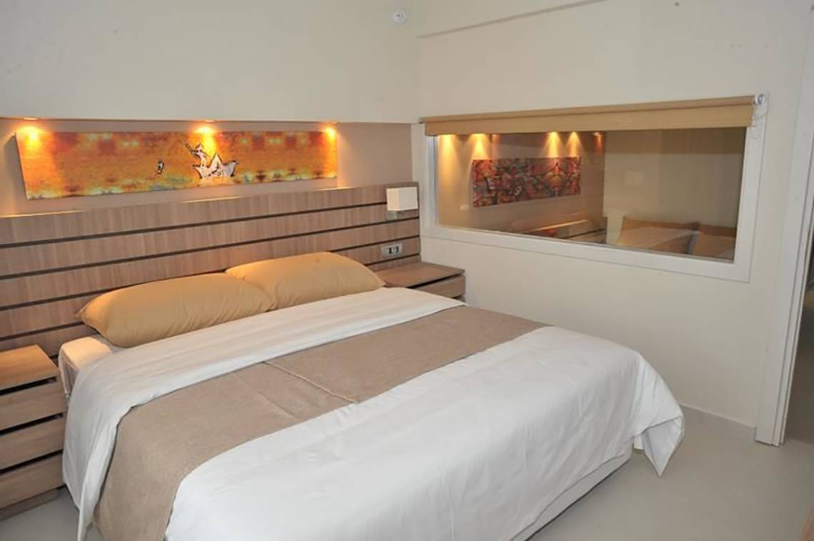 Ein Schlafzimmer im Atlantica Holiday Village Kos mit einem Bett, zwei Nachttischen und einem großen Fenster.