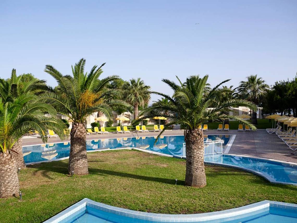 Außenpool des Atlantica Holiday Village Kos mit Palmen und Sonnenliegen.