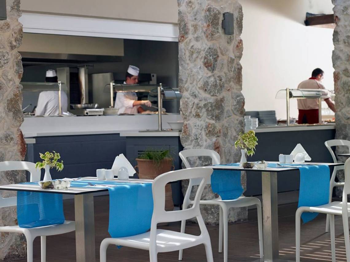 Restaurant des Atlantica Holiday Village Kos mit blauen Tischdecken und Köchen im Hintergrund.