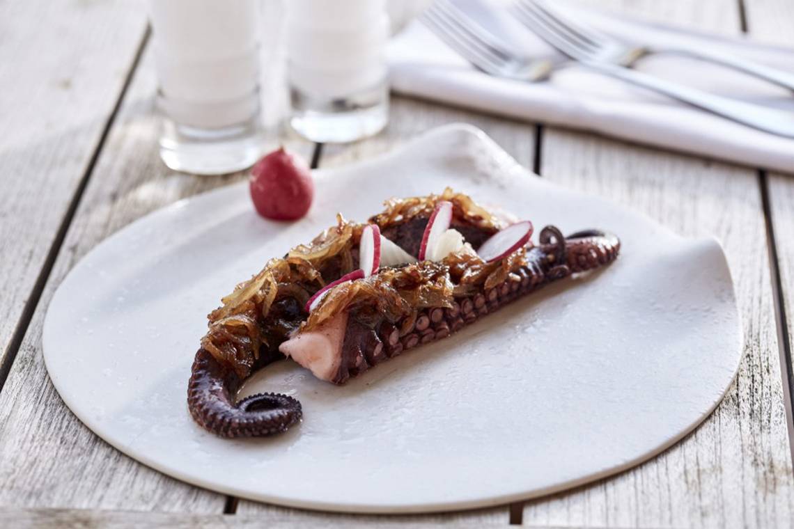Ein Teller mit gebratenem Tintenfisch, Zwiebeln und Rettich auf einem Holztisch.