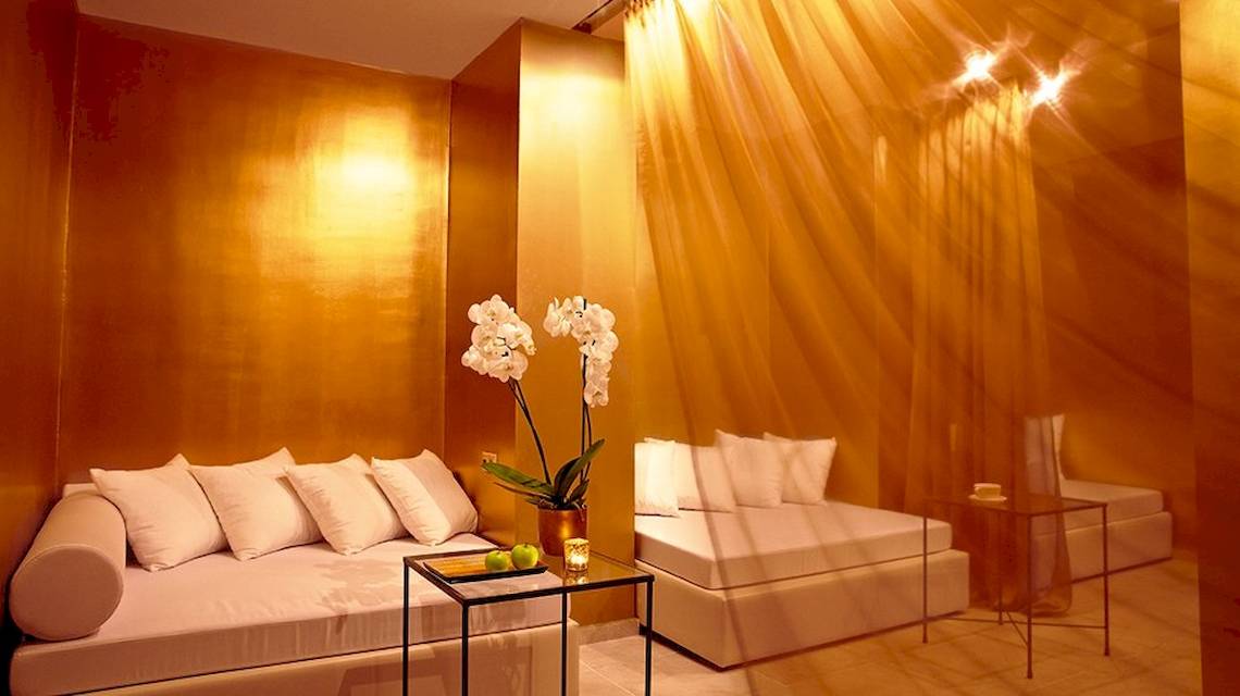 Innenraum des Grecotel Meli Palace mit goldenen Wänden, weißen Möbeln, einem Tisch mit Blumen und Früchten
