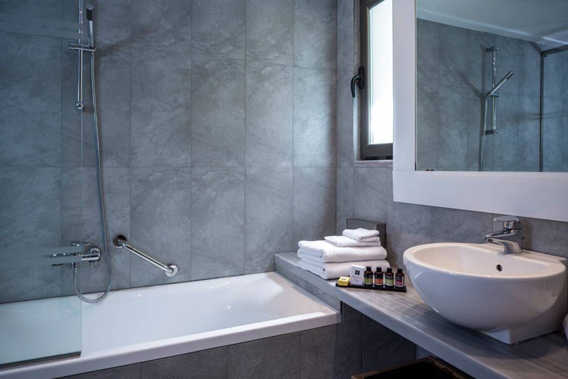 Badezimmer im Kontokali Bay Resort & Spa mit Badewanne, Handtuchstaender, Waschbecken und Spiegel.