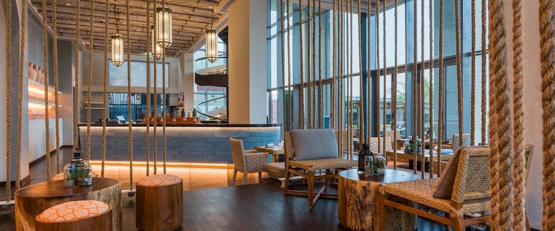 Inneneinrichtung der Lobby im Kempinski Hotel Muscat mit Holztischen, Stühlen und einer Bar.