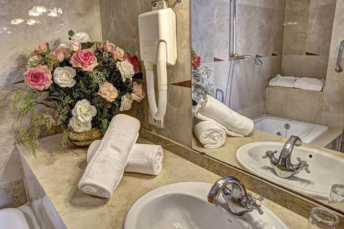 Badezimmer mit Blumenstrauß, Spiegel und Handtüchern im Bull Hotel Reina Isabel & Spa