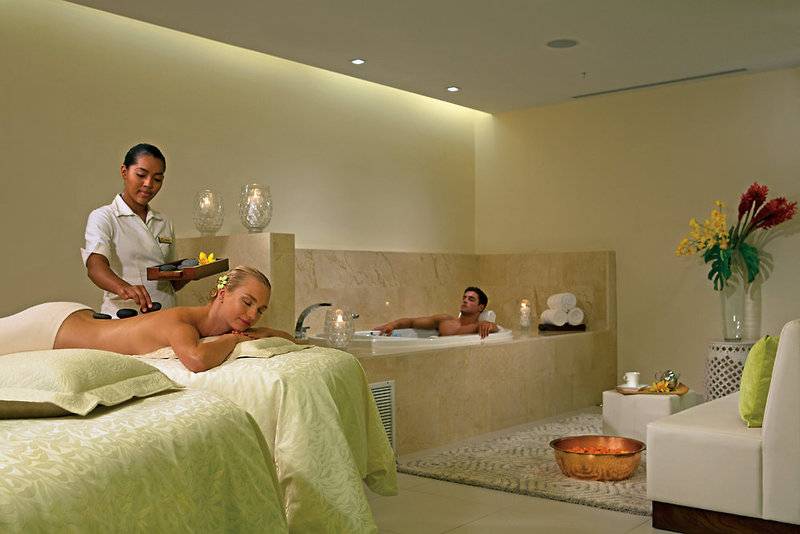 Massagebehandlung im Hotel Dreams Las Mareas Costa Rica mit einer Frau auf einer Liege und einem Mann im Whirlpool.